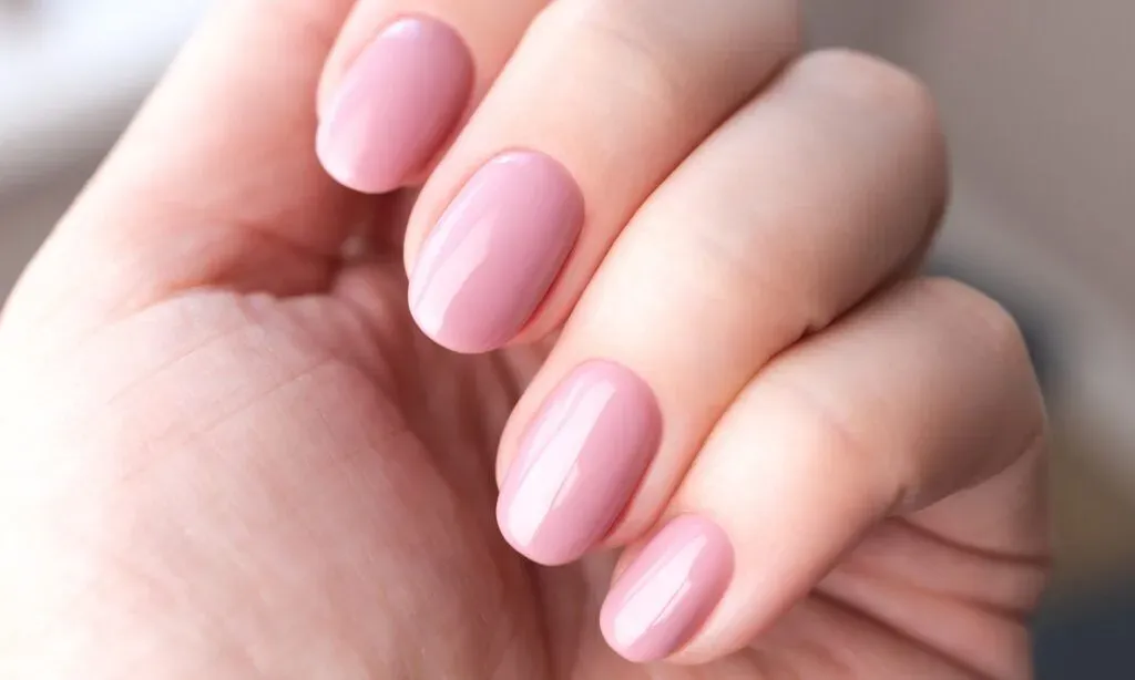 Naturlig ljusrosa gellack målning på välvårdade naglar.